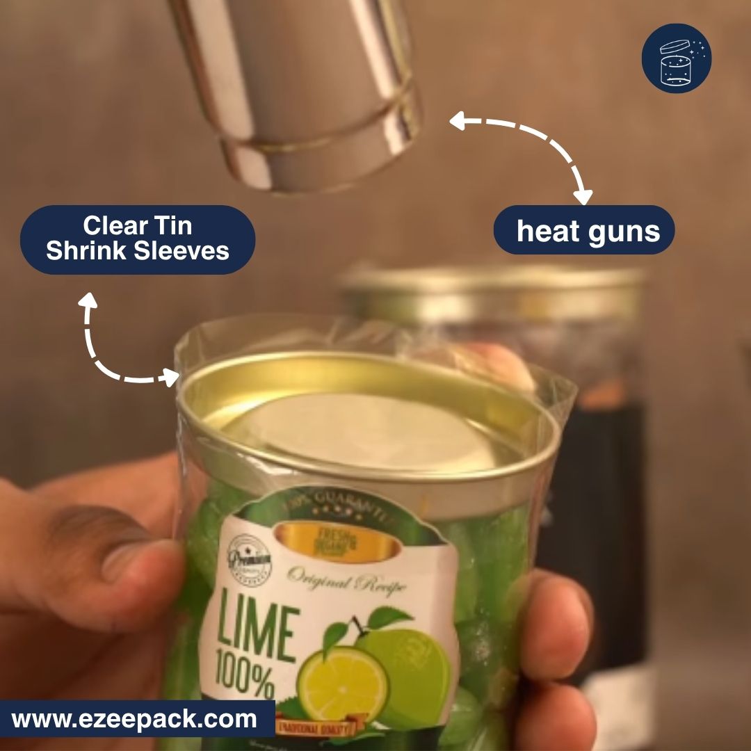 A hand holds a clear-labeled lime-flavored can while a metal heat gun heats the top. Text callouts identify clear shrink sleeves and heat guns, with a website watermark at the bottom.